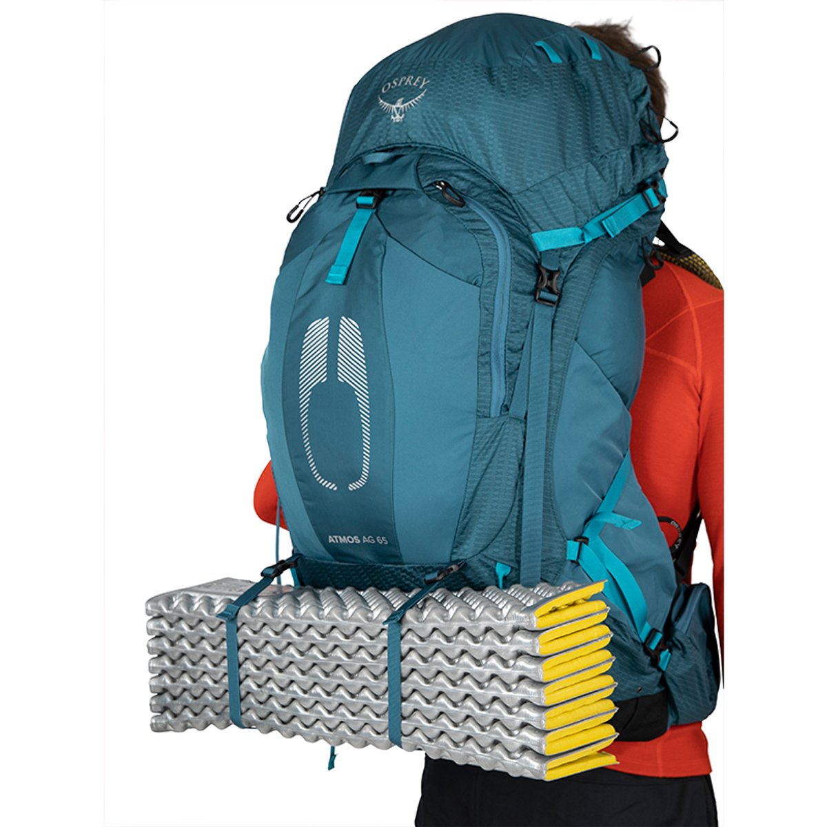 A side view of a person wearing a blue Osprey Atmos AG 65 backpack with a silver and yellow closed-cell foam sleeping pad strapped to the bottom using the external attachment loops.