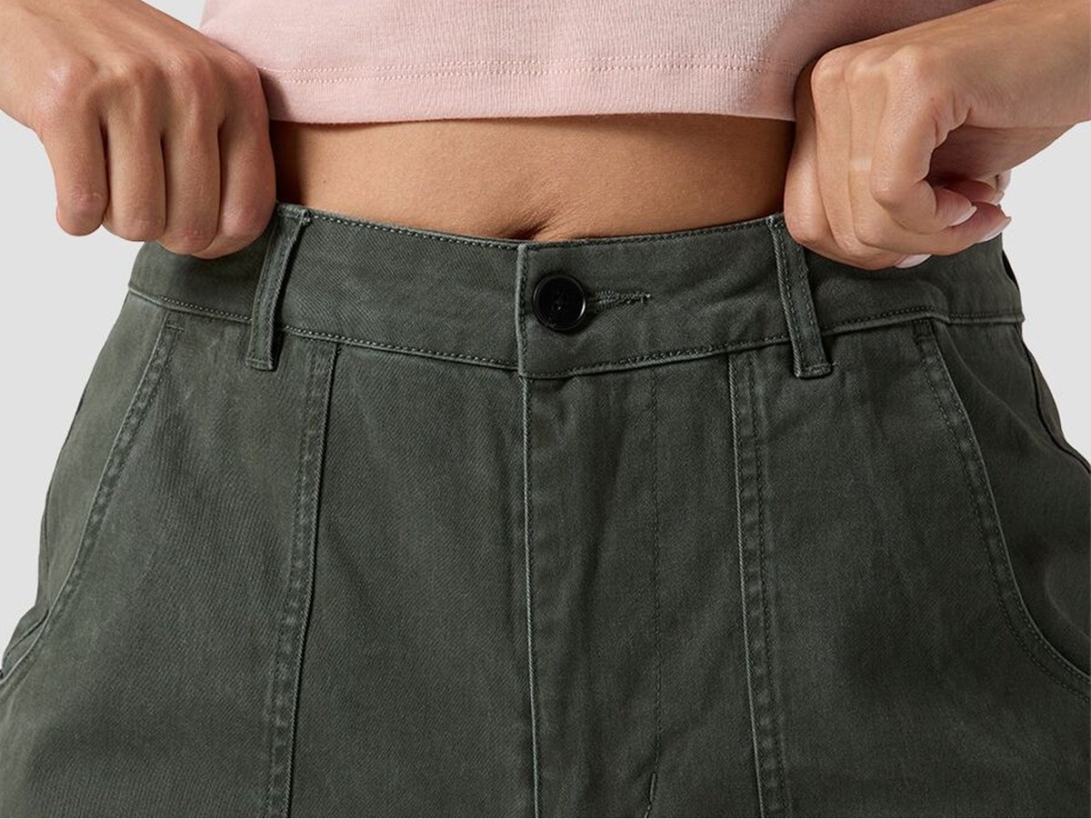 Close-up of a person wearing high-waisted olive pants with front pocket seams, a button closure, and belt loops.