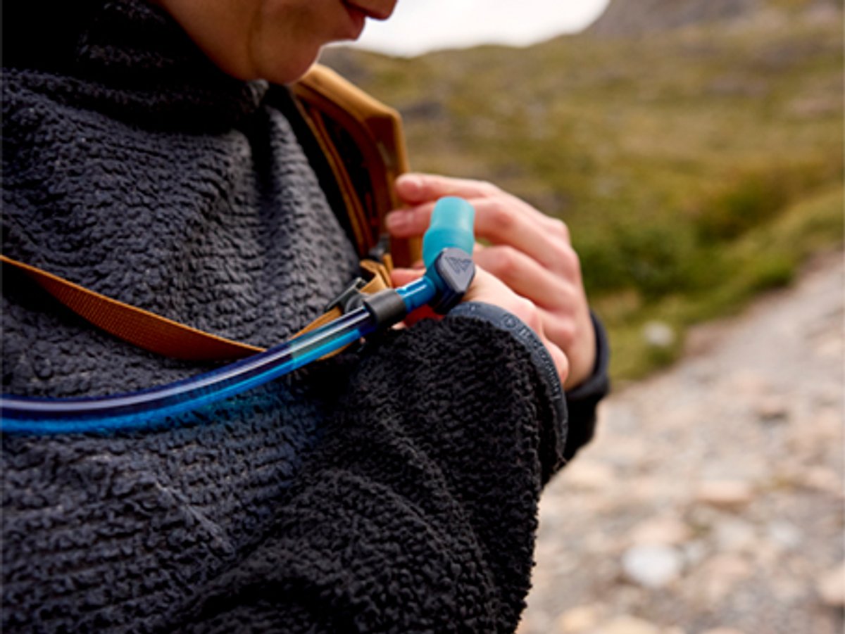 Person wearing fleece jacket adjusting their hydation tube and backpack chest strap.