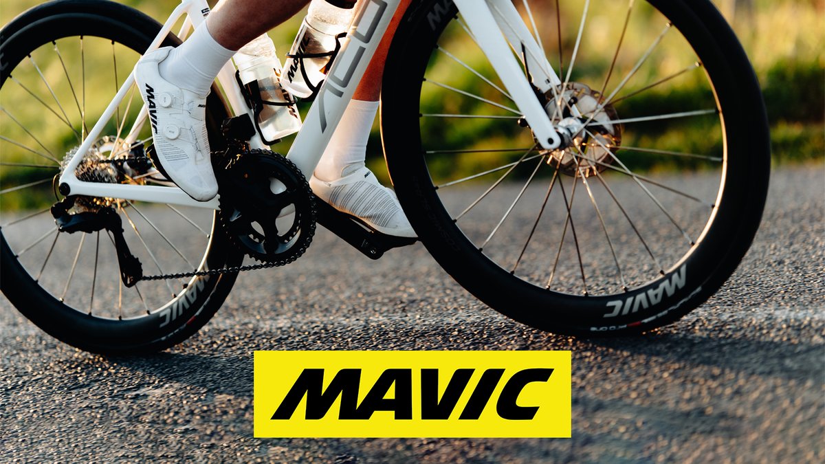 Professional cyclist riding a Mavic wheelset road bike outdoors wearing white cycling shoes and gear on asphalt pavement.