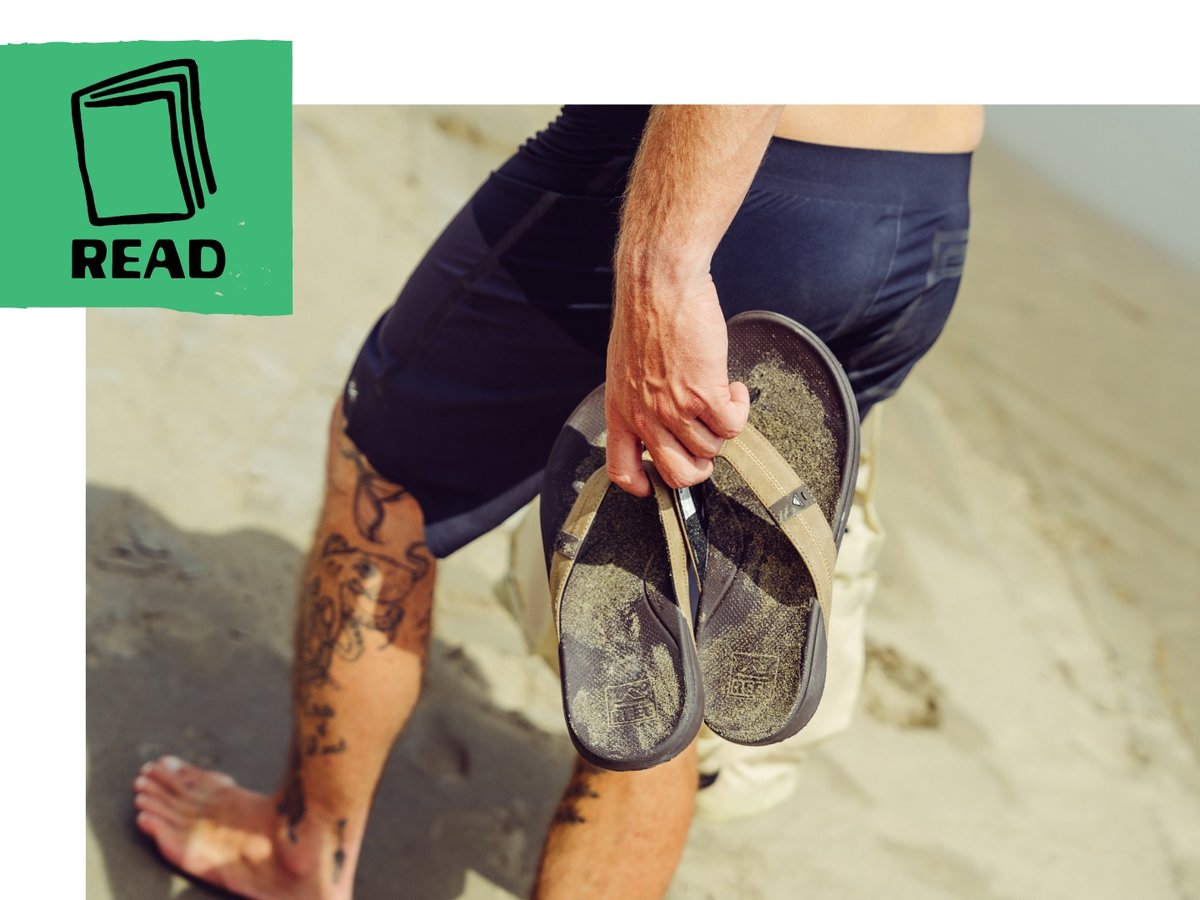 Beach-goer holds sandals on the beach. 