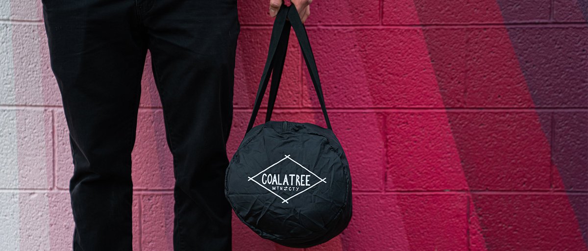 Person holding Coalatree Nomad PAckable Duffel in front of painted mural wall.