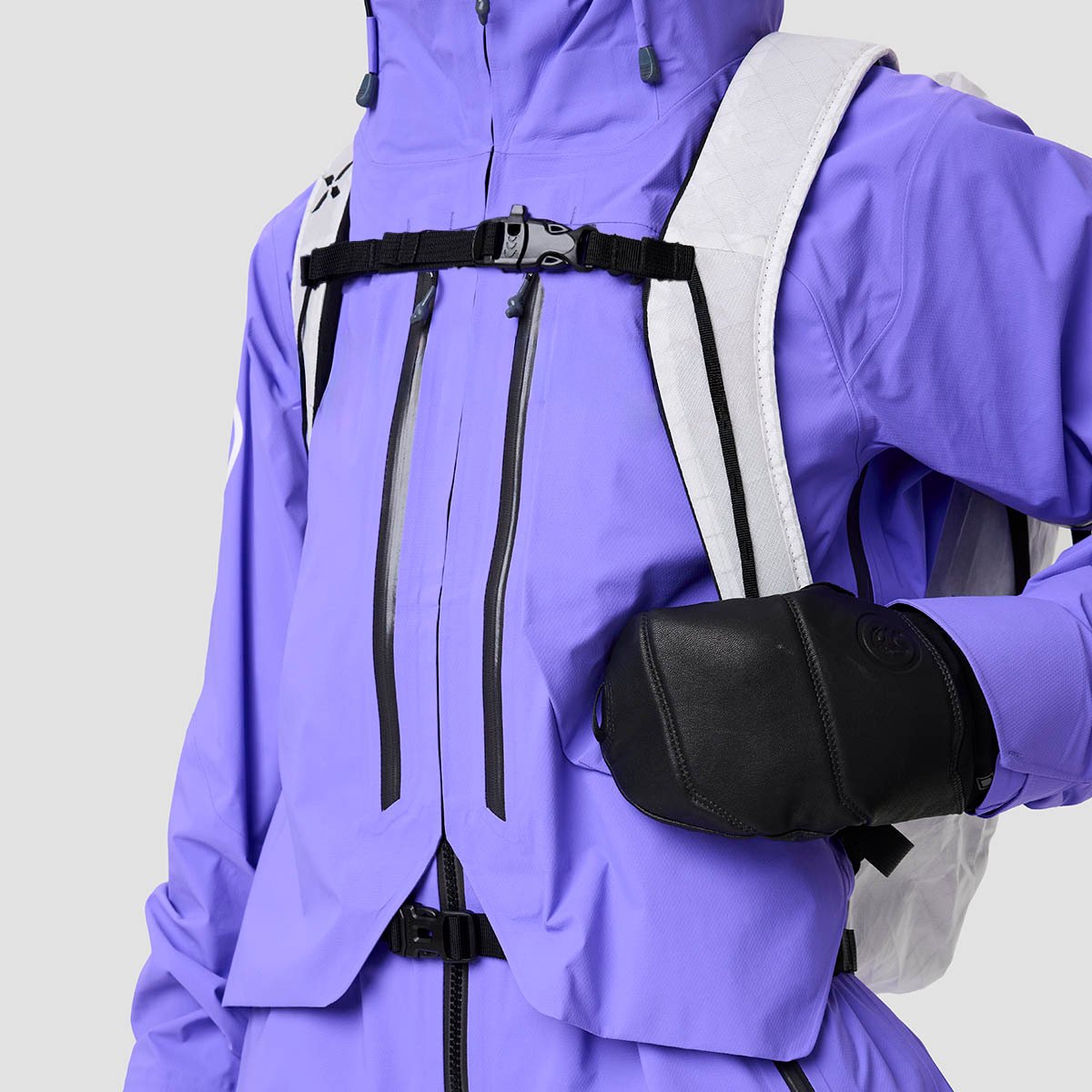 Person wearing backpack over ski shell with waist belt strap laying flat beneath large bellow style chest pockets.