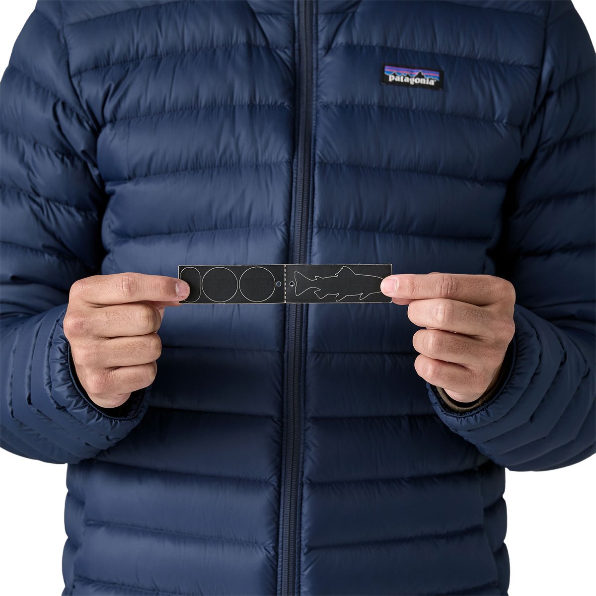 A person wearing the Patagonia Down Sweater Jacket holds repair patches in front of their chest