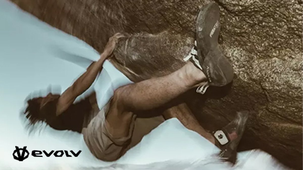 A rock climber wearing specialized Evolv climbing shoes scales a vertical rock face from an overhead perspective.