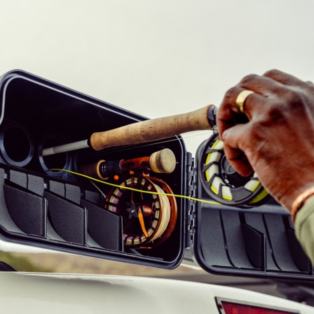 A fisherman pulls a fly fishing rod out of its vehicle-mounted case. 