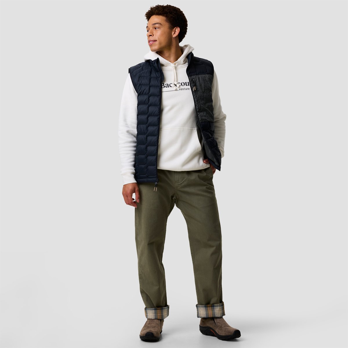 Men's navy quilted gilet layered over white hoodie with olive chinos and suede boots, showcasing casual layered styling.