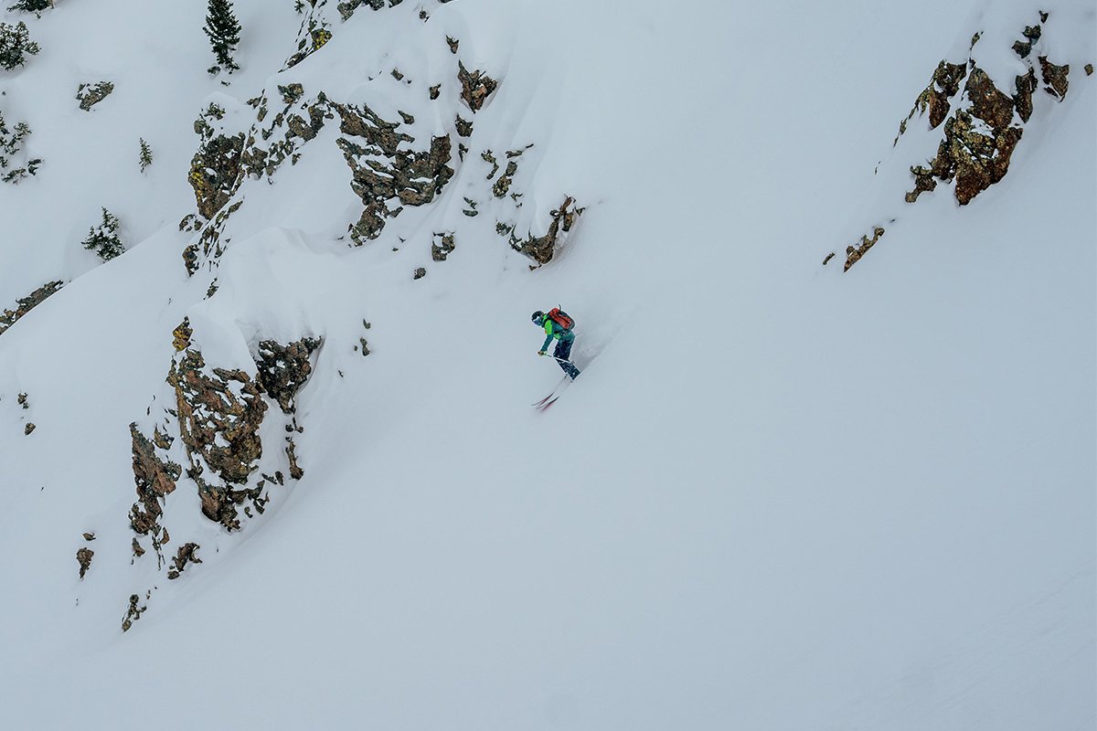 Skiier carving down steep rocky mountain face wearing avypack.