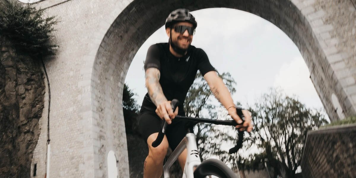 Cyclist riding Ridley Falcn bike under stone arch.