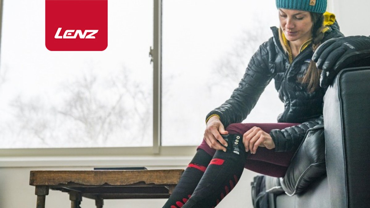 Woman in winter athletic gear putting on Lenz heated socks before skiing, showcasing thermal clothing for cold weather sports and outdoor activities.