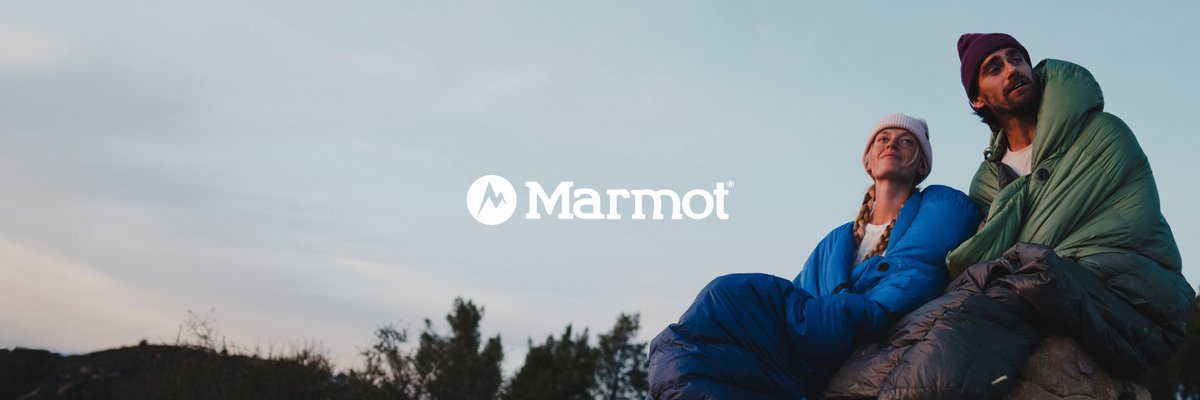 A man and a woman wrapped in sleeping bags watching a sunset at camp.