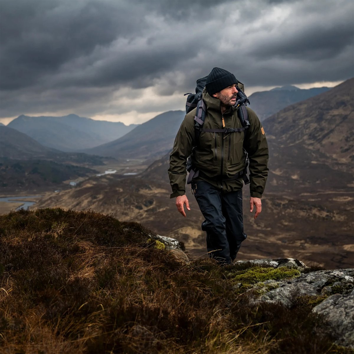 A man walks along a cloudy slope, wearing Fjallraven Keb trekking gear.