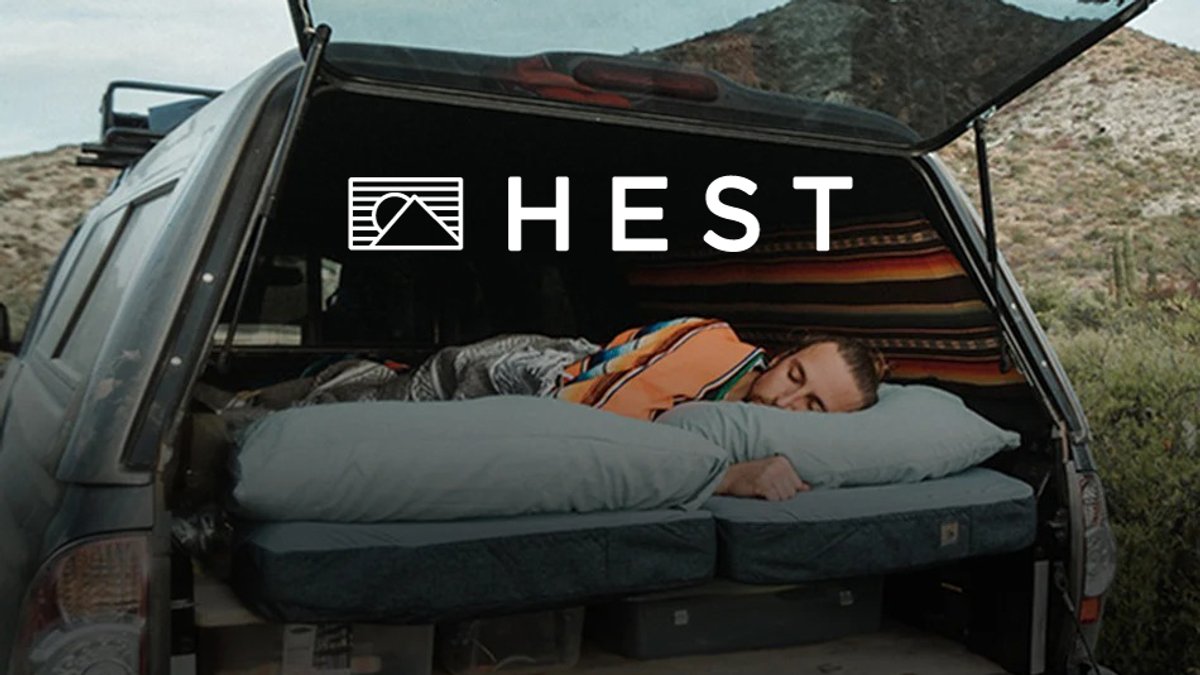 Man sleeping comfortably on a HEST truck bed camping pad in the back of a pickup truck in a desert landscape setting.