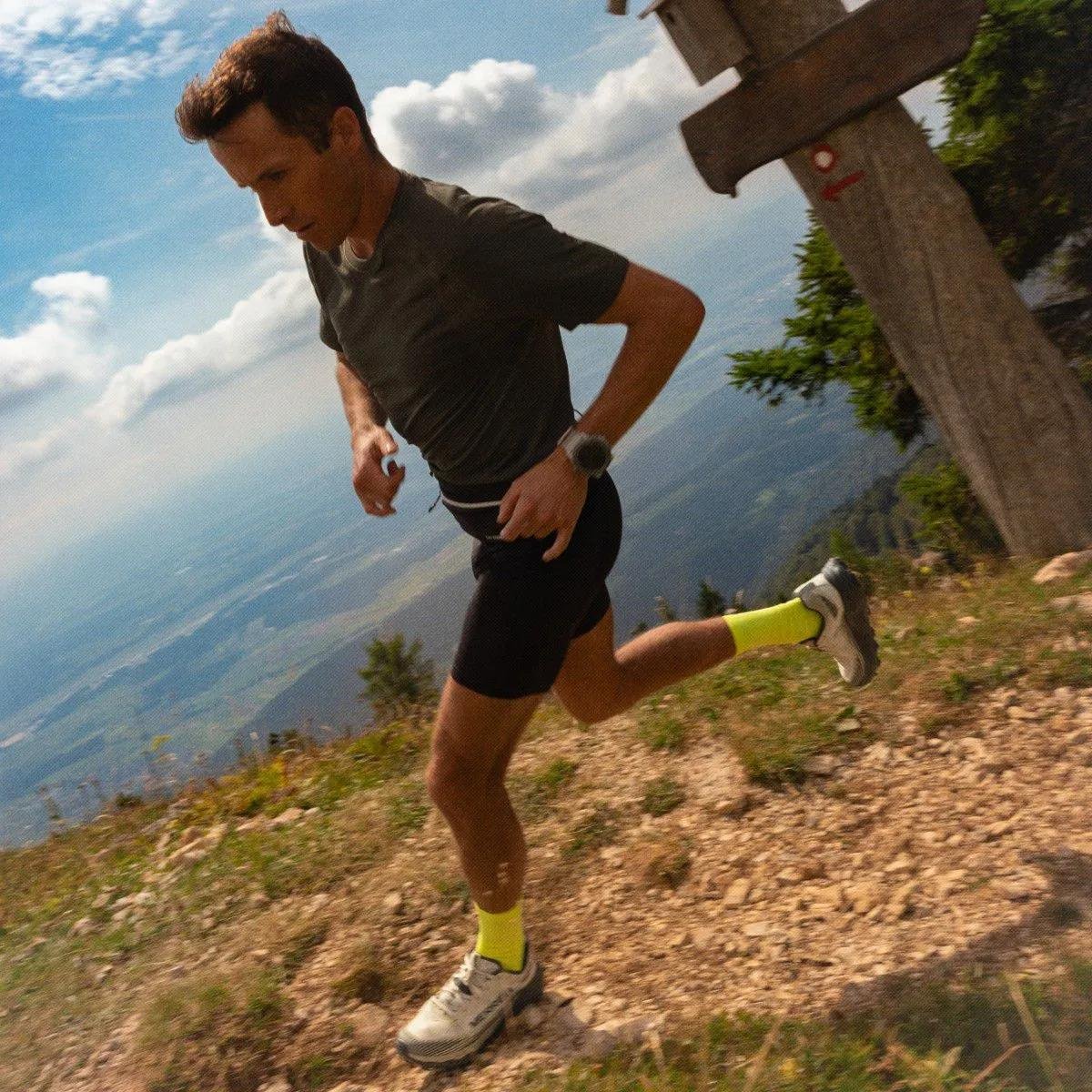 Runner sprinting up a rocky hill in profile with the sky behind them.