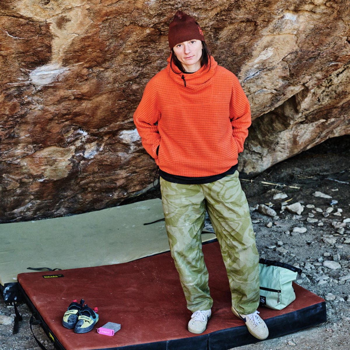 A person wearing a Summit Fleece stands on a crash pad beneath a rock.