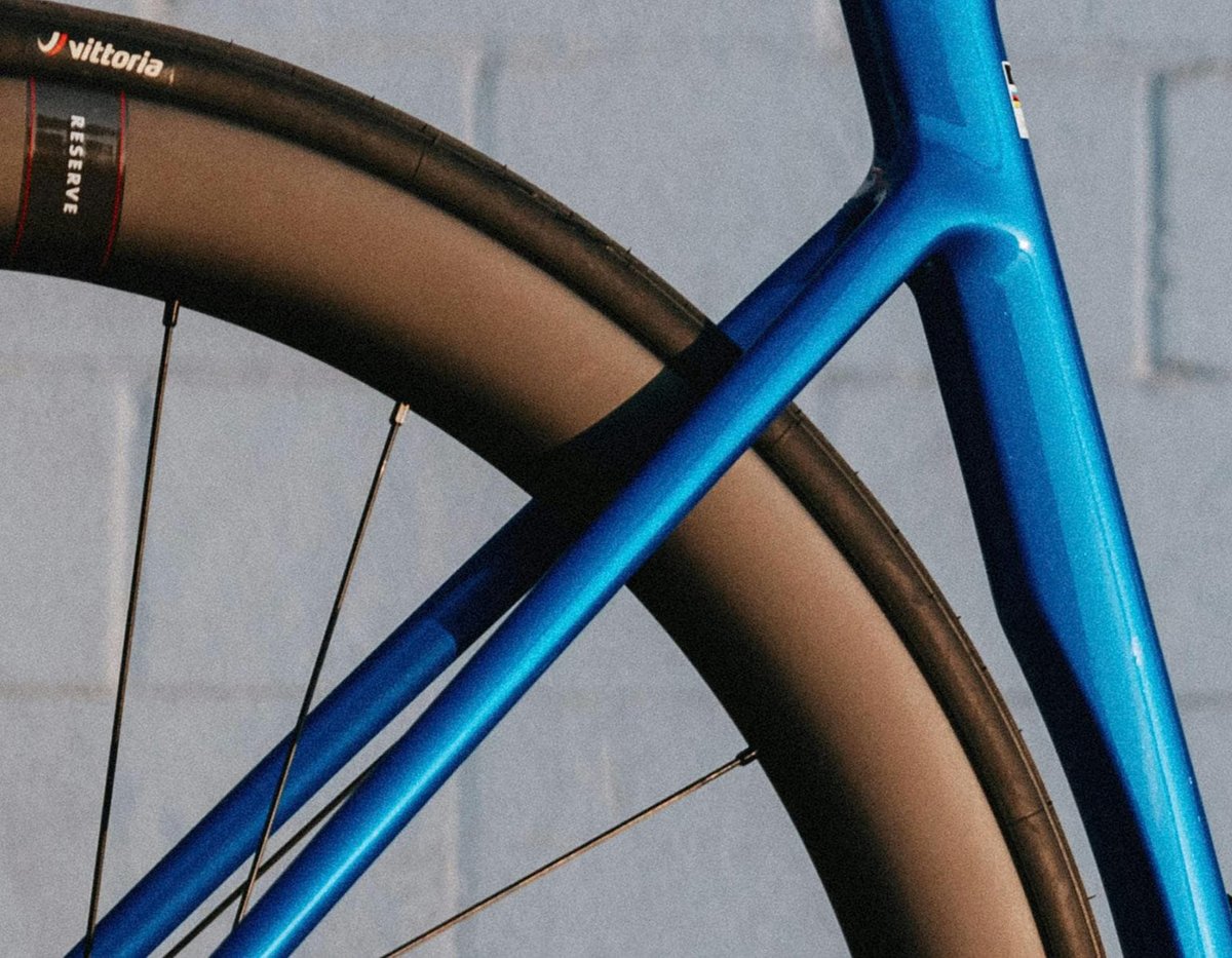 Close-up of blue carbon road bike frame seat stay junction with Reserve carbon wheelset and Vittoria road tire detail
