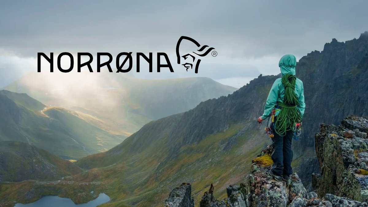 A climber with green rope coiled on their back stands on a rocky peak overlooking a dramatic valley under the Norrona logo.