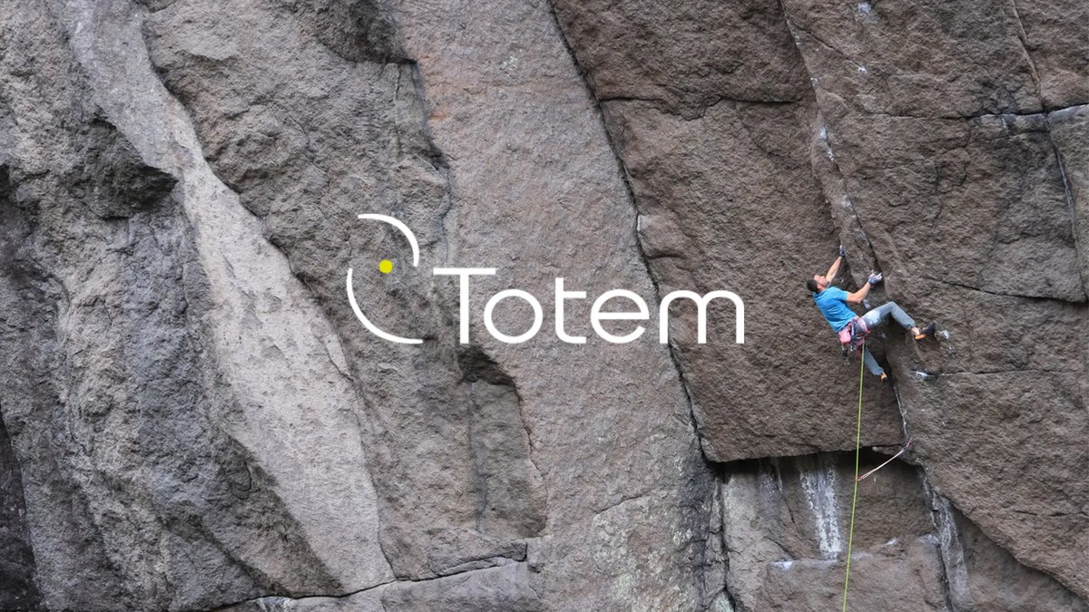 Professional rock climber in blue shirt ascending granite cliff face with yellow rope and safety equipment during outdoor climbing adventure.