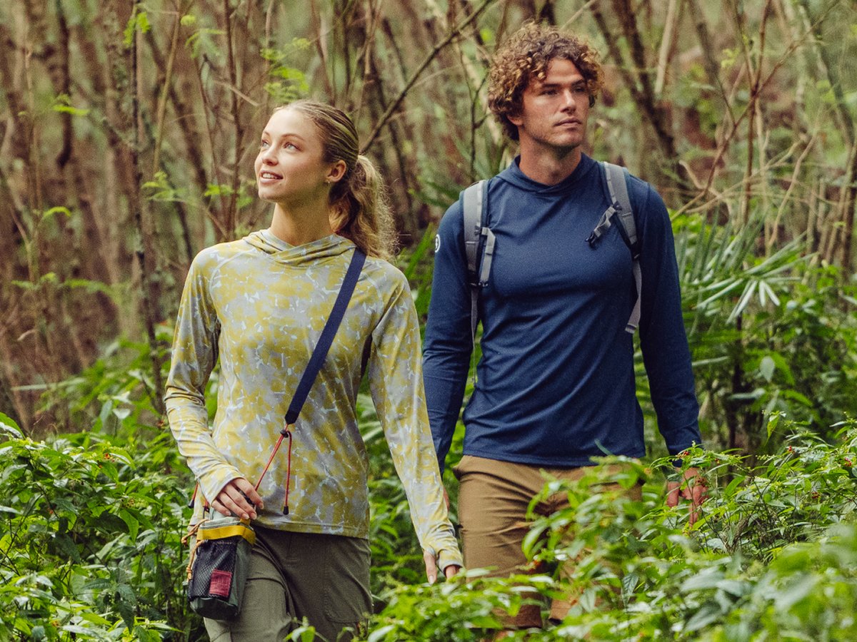 Two people hike through a very green forest.