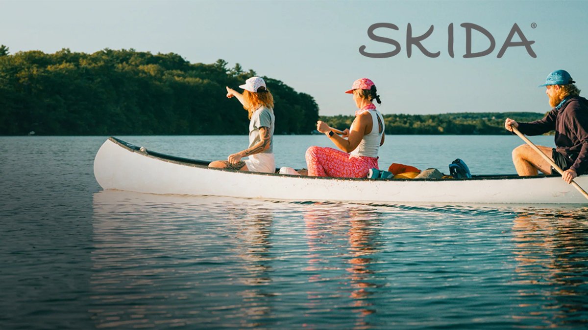 Three people sit in a white canoe on calm turquoise water with forested shoreline in the background under clear skies.
