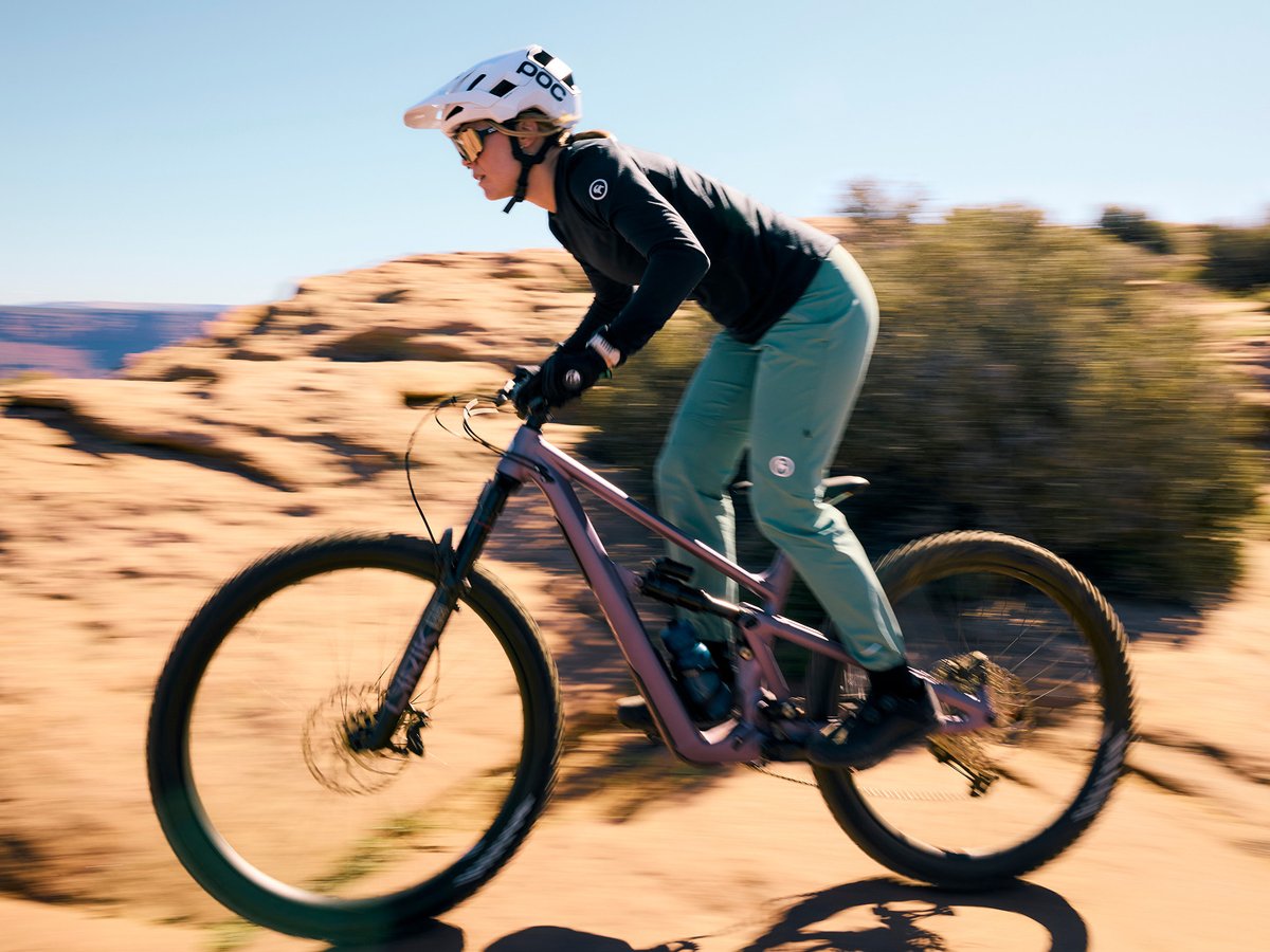 Woman riding a full-suspension mountain bike through a desert trail in Backcountry MTB apparel.