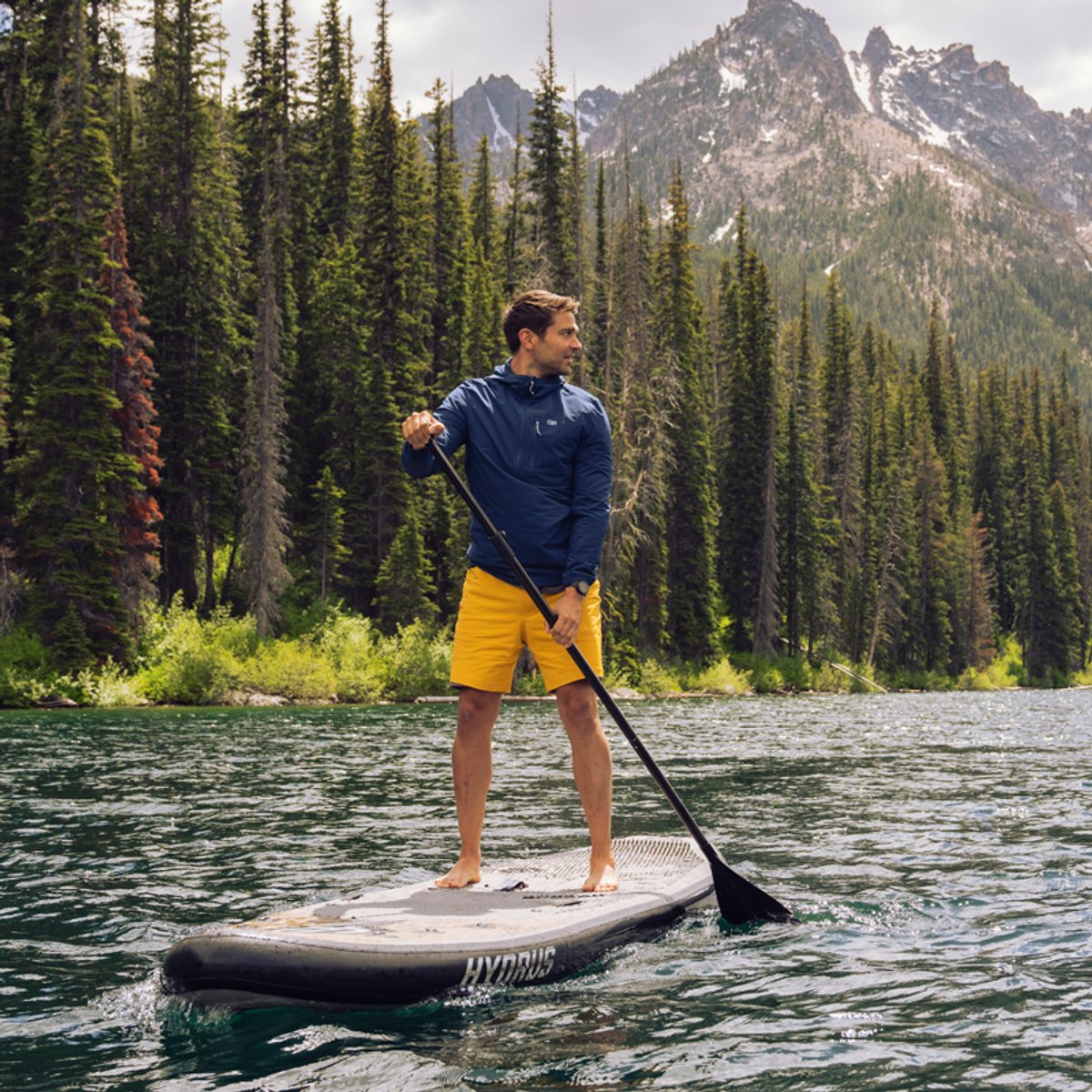 A man wearing Ferrosi shorts paddleboards on an alpine lake.