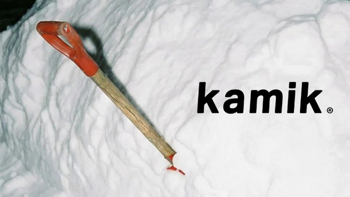 Kamik brand wooden-handled shovel with red ferrule resting inside of snowbank.