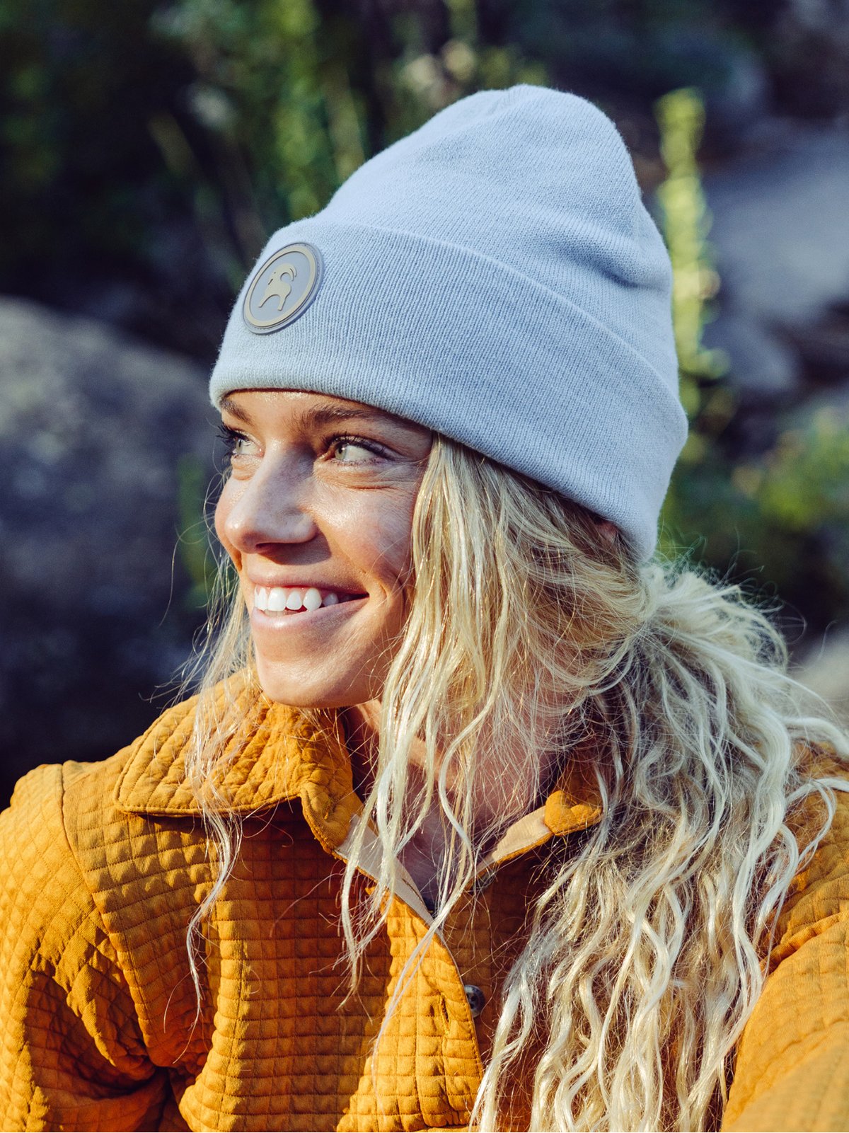 A woman with long curly blonde hair is wearing a folded beanie with a round goat patch.