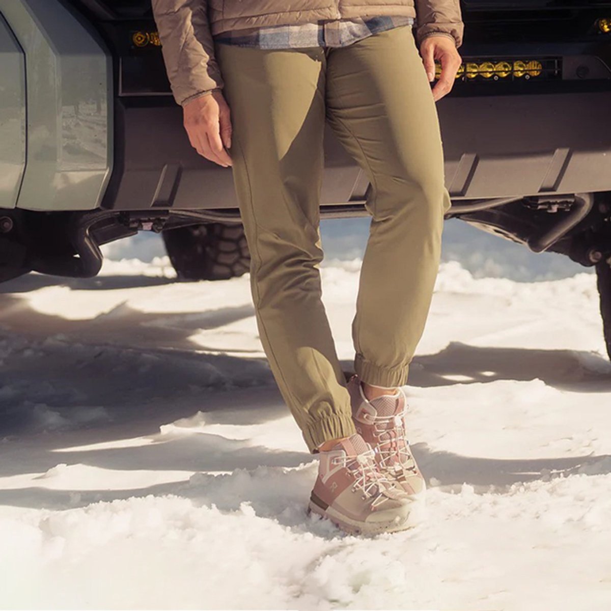 A woman wearing Ferrosi Joggers leans against a vehicle parked in the snow.
