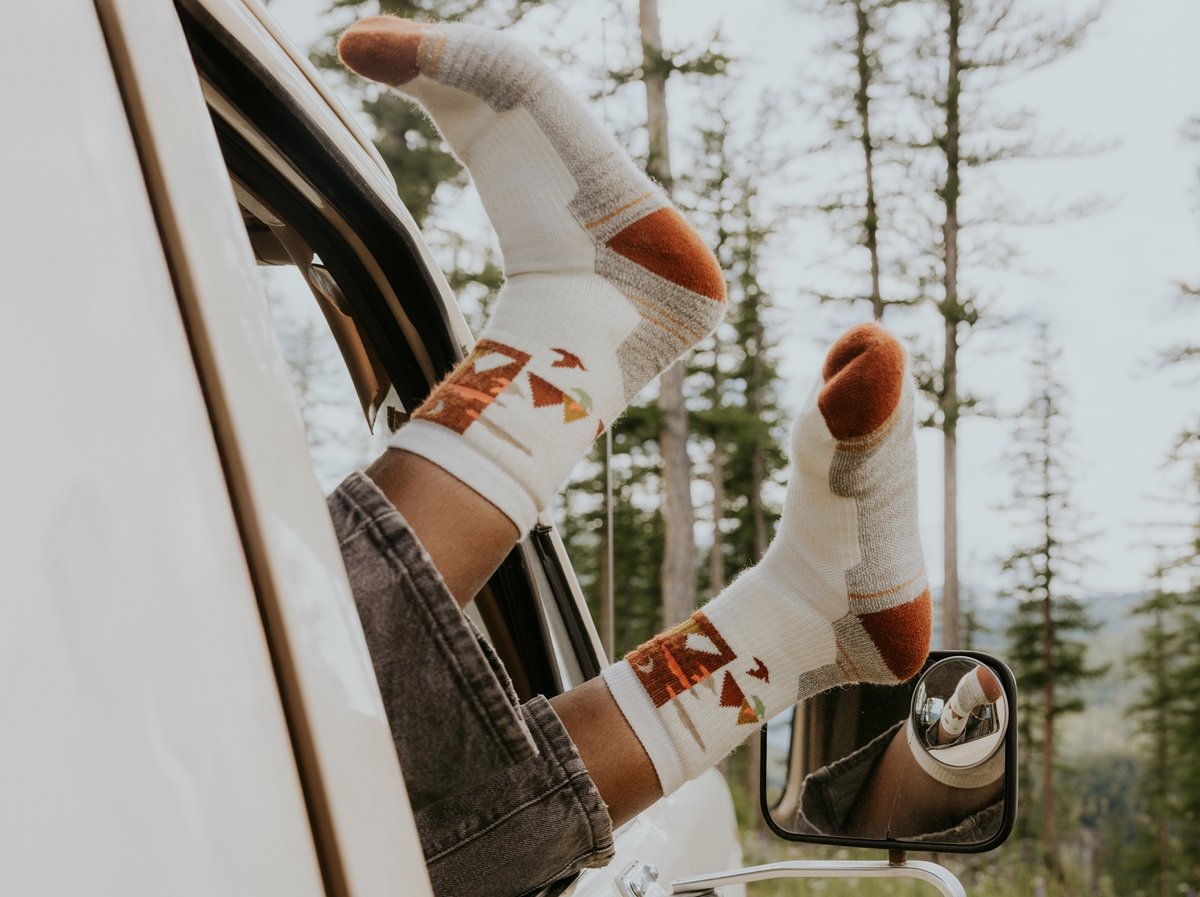 A person’s feet are hanging out an open car window. They are wearing colorful socks.