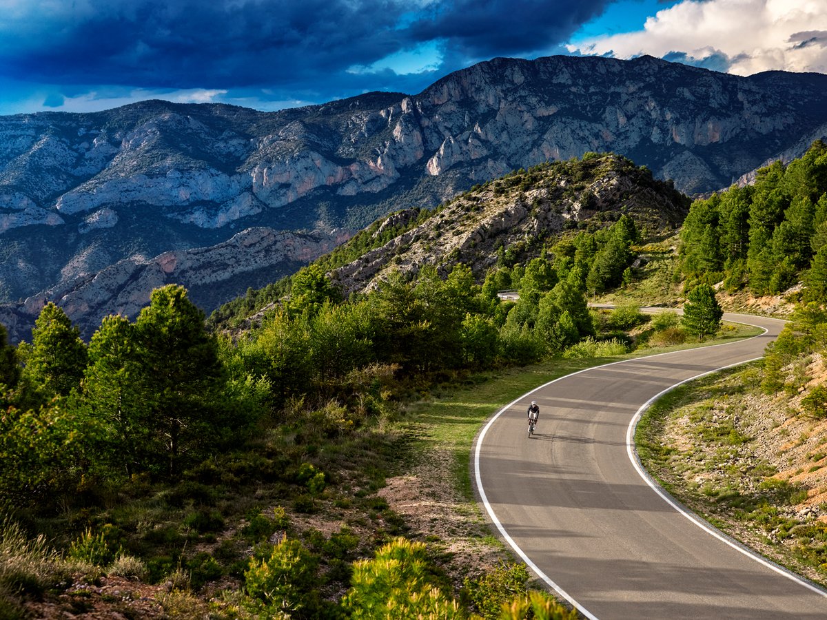 An aerial view of a roadbike rider going downhill against a rocky mountain backdrop.