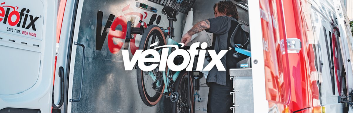 Mechanic working on a bike mounted in a repair stand inside the open rear of a mobile service van, featuring the Velofix logo.