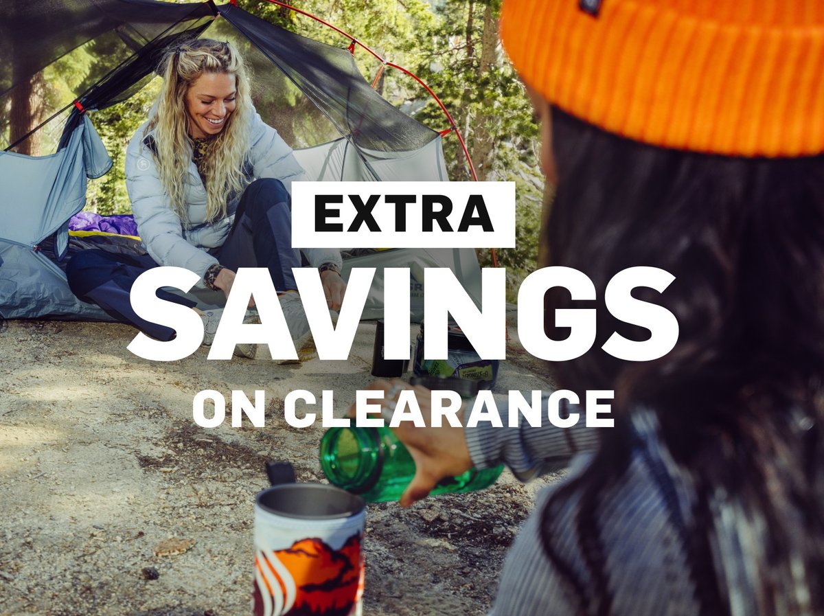 Two people relaxing at a forest campsite with a tent and camp mug. Extra savings on clearance.