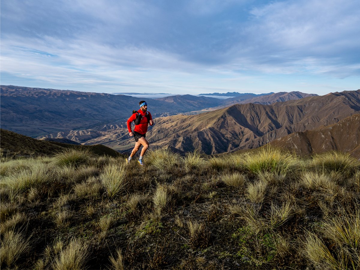 A man wearing a running vest runs along a mountainous ridge, wearing a Garmin Enduro 4.