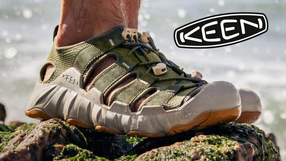 KEEN waterproof hiking sandal with olive and cream colorway displayed on a mossy rock near water, showcasing durable outdoor footwear design.