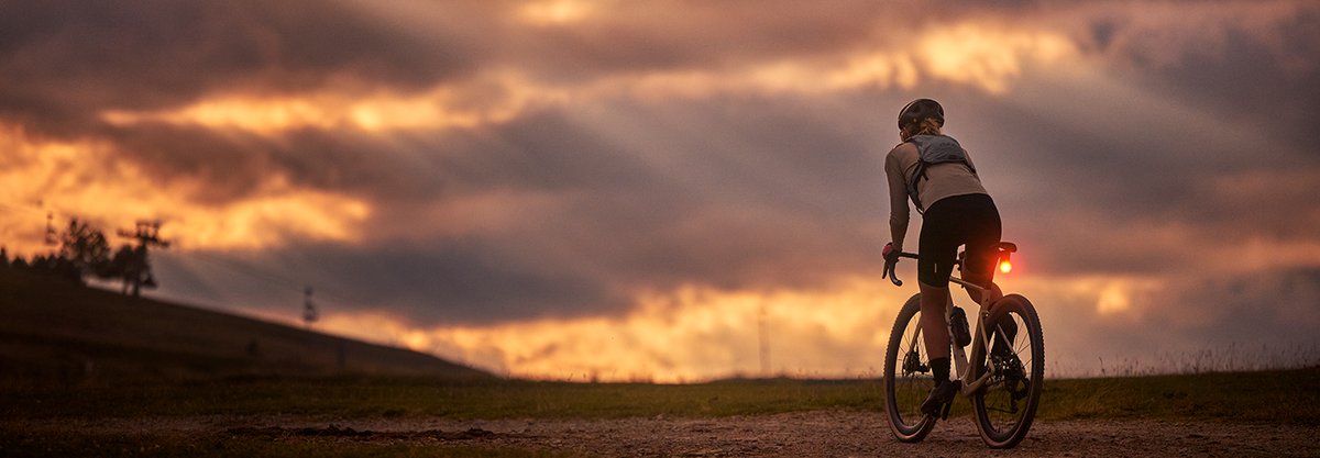 Rider on a gravel bike at sunset with rear light glowing on open trail