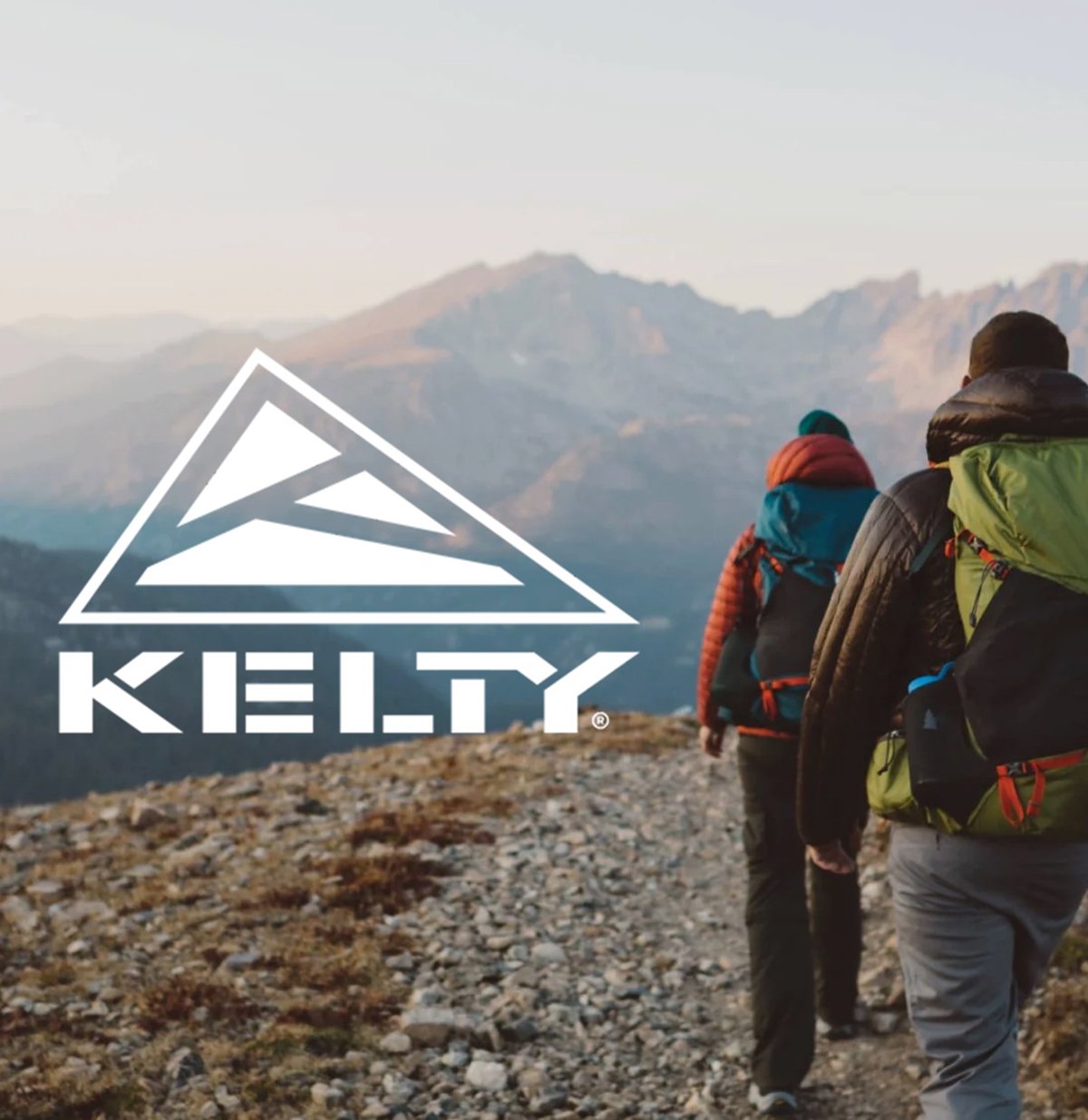 Two backpackers walk along a beautiful mountain ridge. Kelty brand logo.
