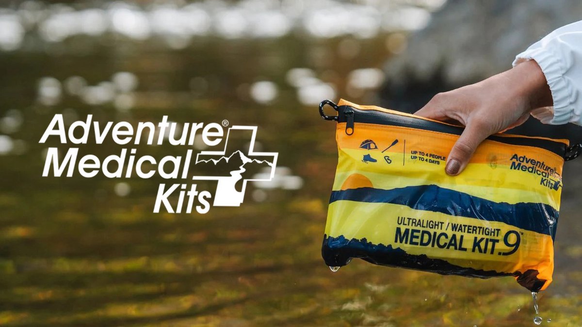 Adventure Medical Kits ultralight waterproof medical kit being held over water during outdoor adventure, showing yellow and blue packaging with water droplets.