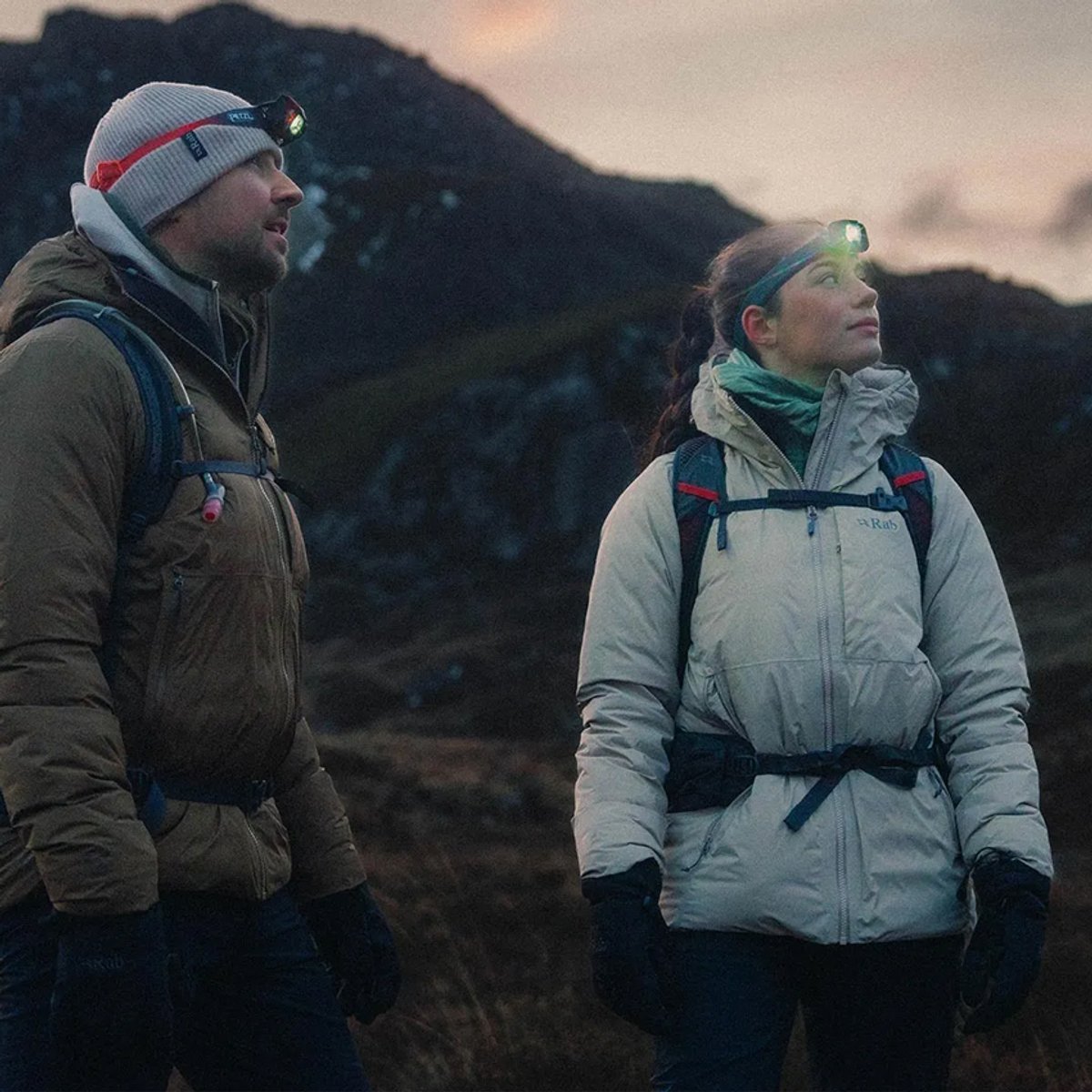A man and a woman stand on an alpine ridge, each wearing Rab Microlight jackets.