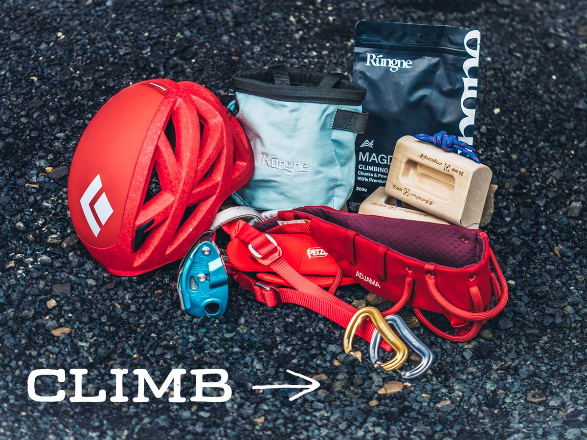 Climbing gear, including a helmet, harness, belay device, carabiners, chalk bag, and a hangboard block, on dark gravel: “Climb.”