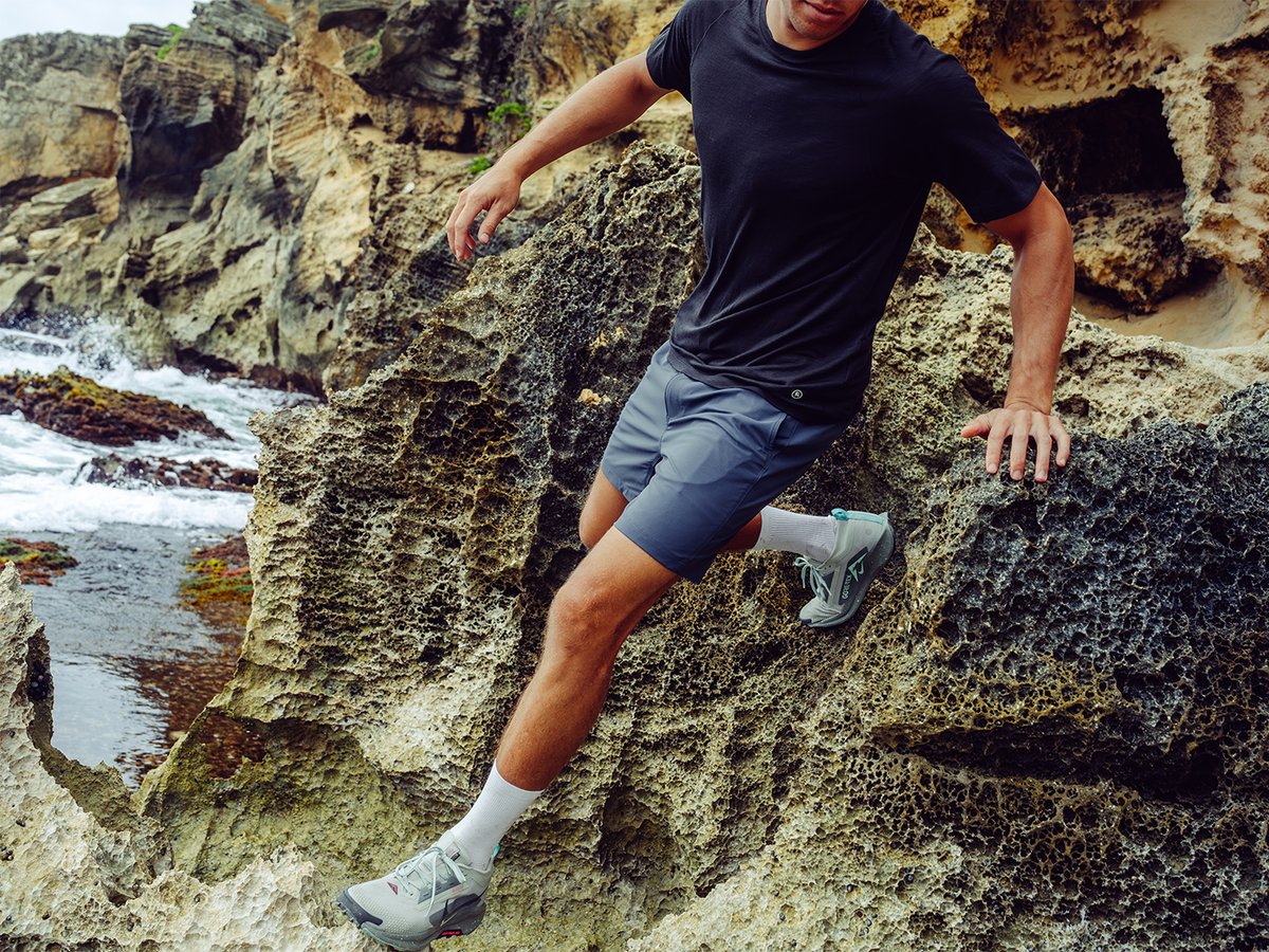 Person scrambling over rocky coastline boulders wearing ripstop shorts.
