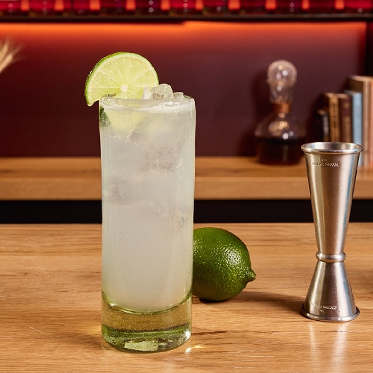 A bar countertop displays a tall glass of gin rickey with ice and a lime wheel, a blue bottle of High West Mountain Gin, an empty bottle of club soda, a jigger, and a fresh lime, set against shelves of liquor bottles; large text reads "Gin Ricky" and the top shows High West Distillery and Backcountry logos.