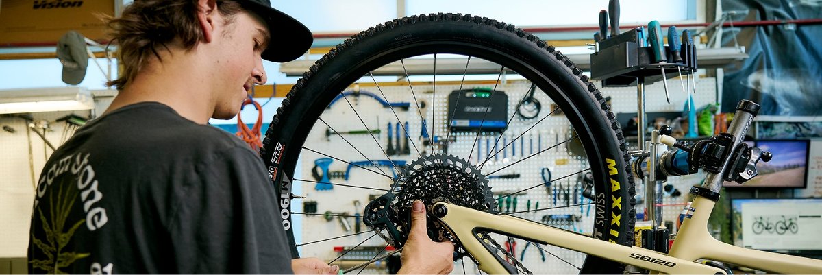 A man in a bike shop stands over a bike frame. He’s looking at the camera with a face that says, “I can build any bike, try me.” 