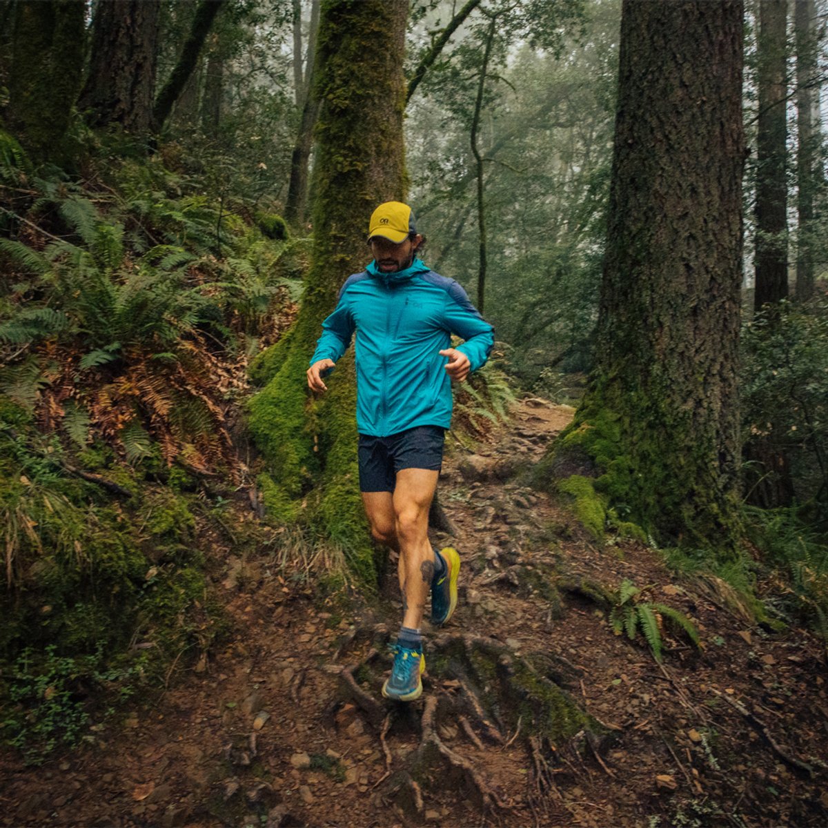 A man wearing a Ferrosi hoodie runs through a rainy forest.
