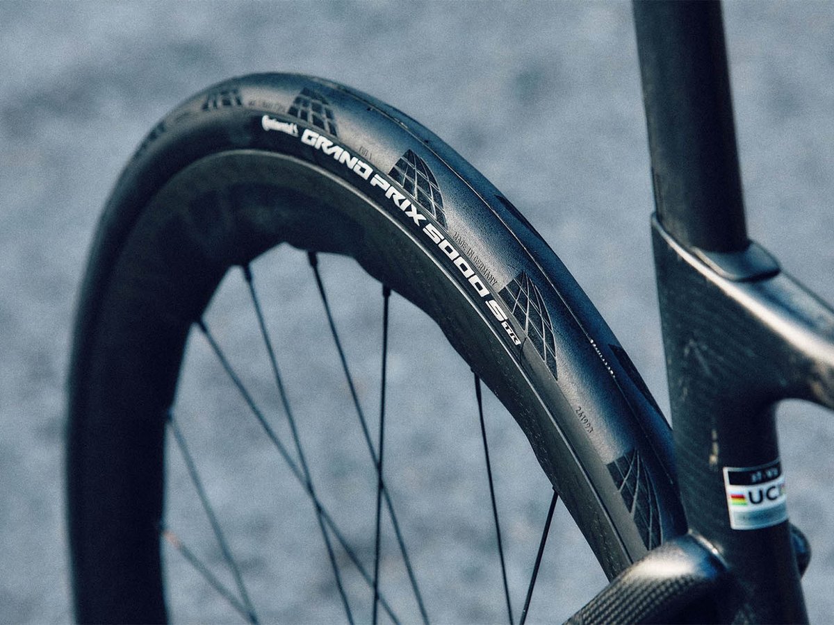 Continental Grand Prix 5000 S TR tire on a deep-section carbon wheel installed on a road bike, angled shot on gray pavement with carbon fork.