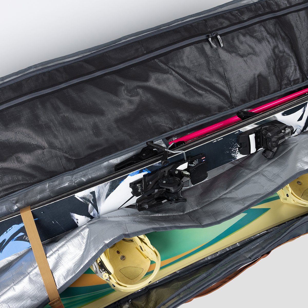 Close-up ski bag interior padded divider flap spearating a pair of skis and a snowboard.