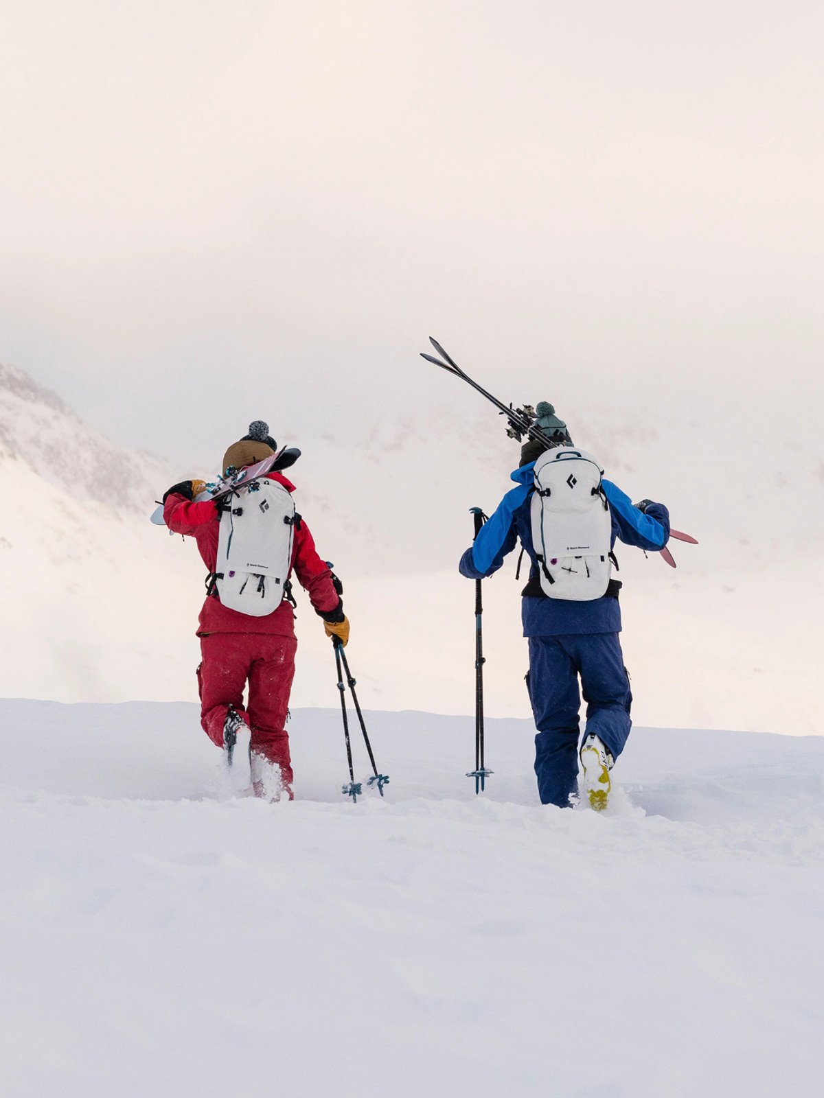 Two skiers walk through deep snow, carrying skis over their should and wearing Black Diamond Recon.