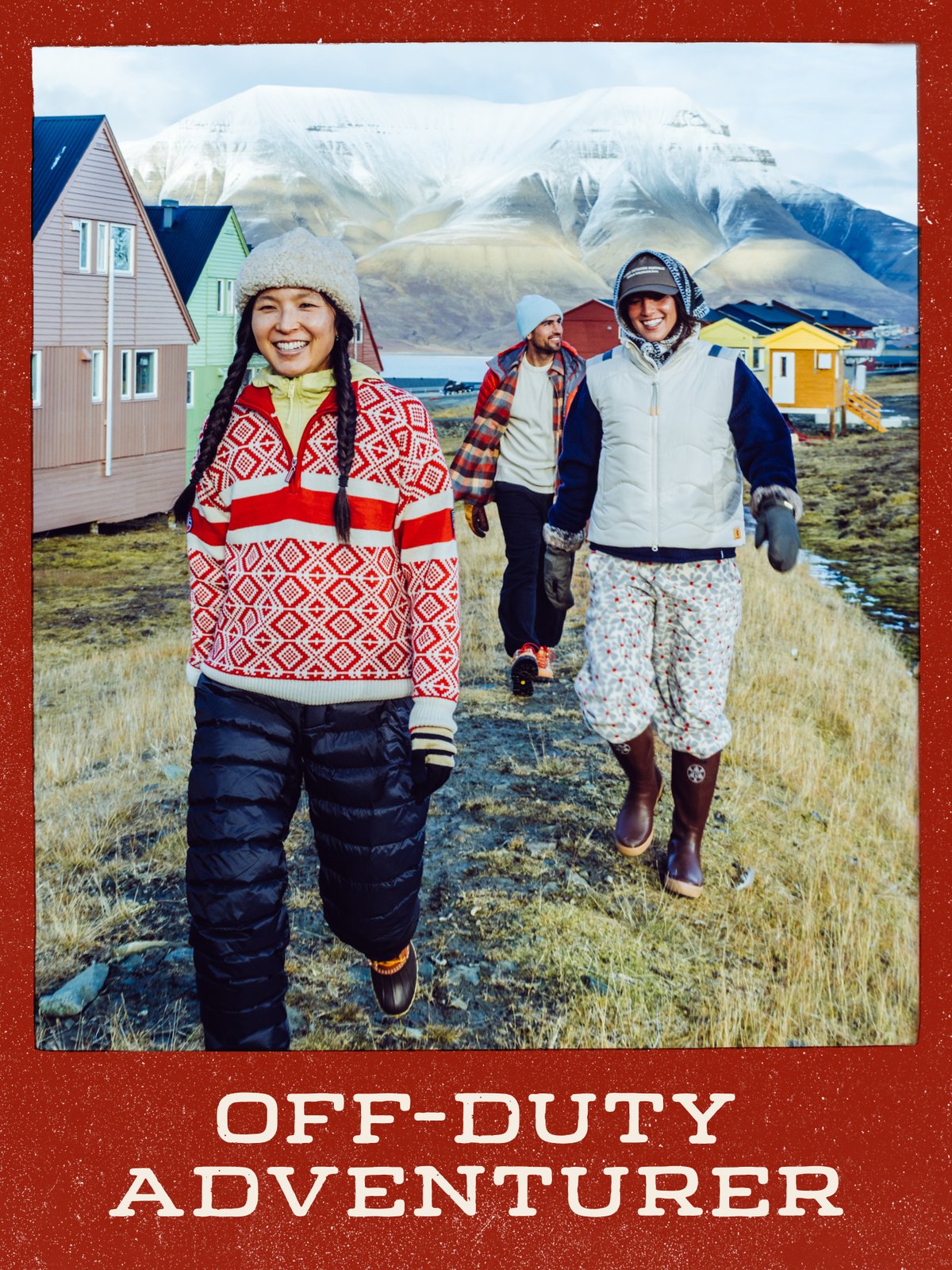 Three friends walking a grassy path past colorful wooden houses, with a snow-dusted mountain behind them: “Off-Duty Adventurer.”