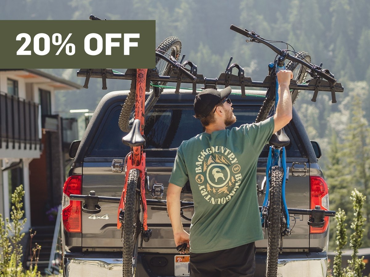 A man fixes his pads on a mountain bike.  A promotional flag says 20% off in the top right corner.