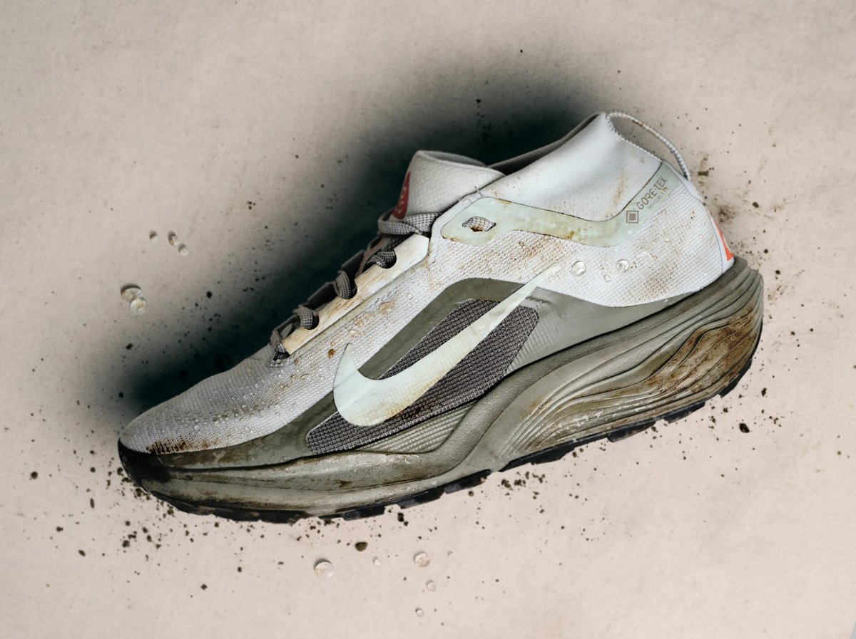 Mud-caked Nike Pegasus GTX trail running shoe with chunky midsole, surrounded by dirt splatter and water droplets on a light surface.